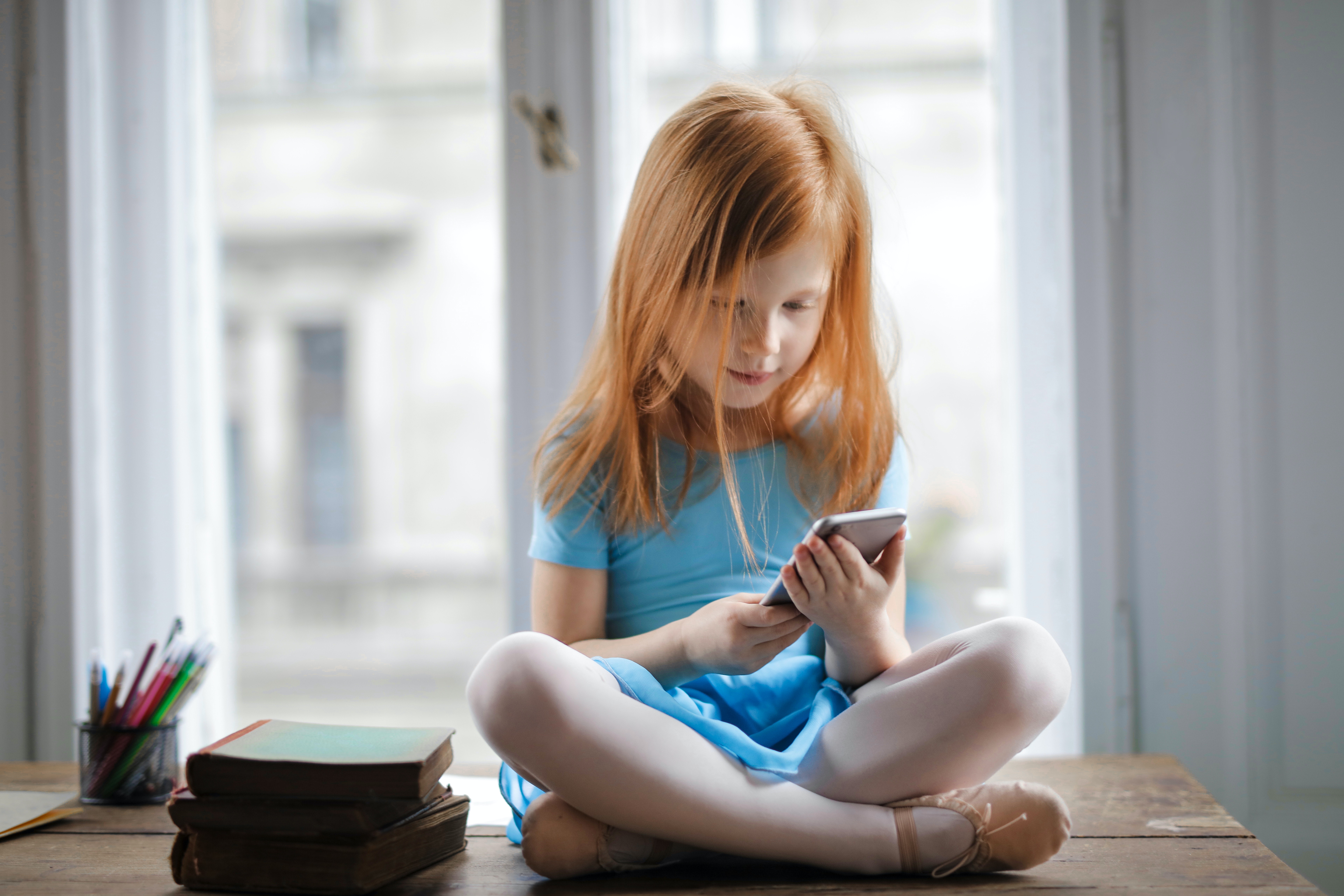 fille assise près d'une pile de livres et regardant son téléphone 